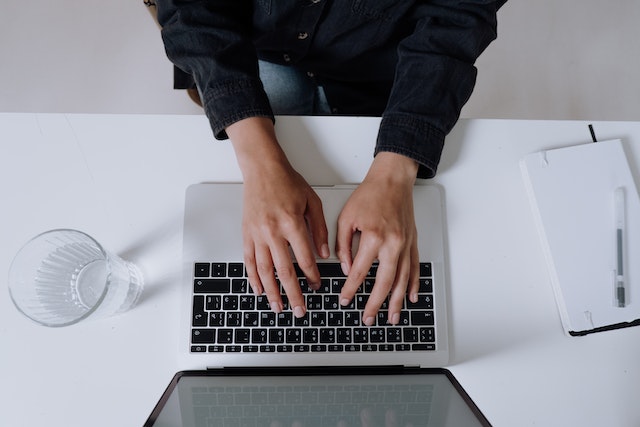 person typing on a laptop with a notebook next to them